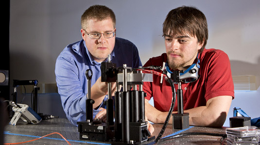 Student and professor work together in physics lab. 